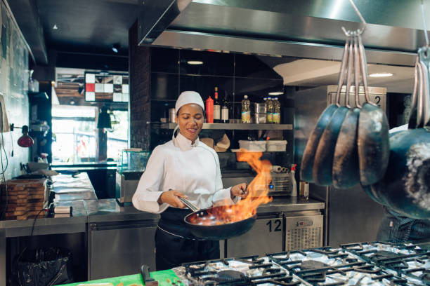 Female chef from the restaurant kitchen is cooking a flambé specialty.